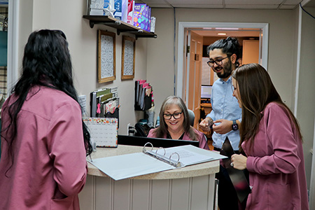 The image depicts a group of individuals, likely employees, wearing matching pink shirts standing behind a reception desk in an office setting.