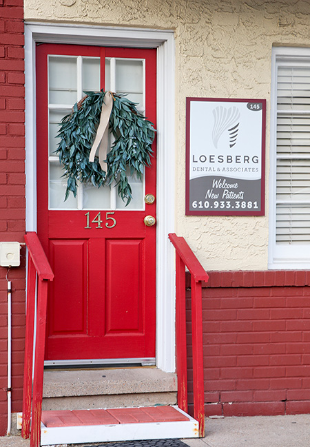 The image shows a red door with a wreath hanging above it, and there s a sign below the wreath with text that includes  Loebsberg  and a phone number.
