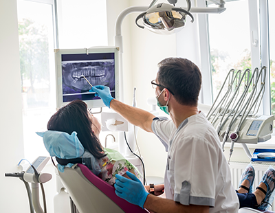 A dental professional examines a patient s mouth with a magnifying glass while seated at a dental chair.