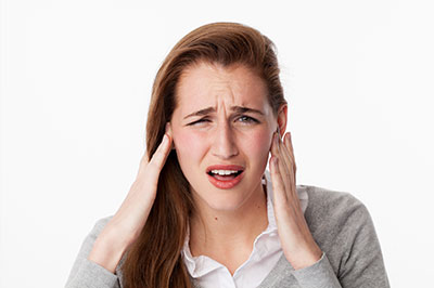 The image shows a woman with her hand on her ear, possibly indicating she s experiencing discomfort or pain, while she appears to be in a state of distress or concern.