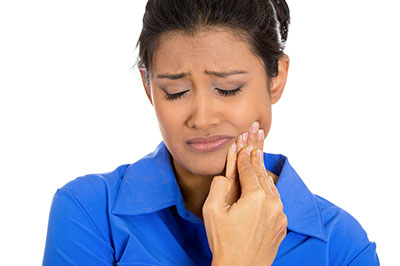 The image shows a woman with her eyes closed, holding her hand up to her face, seemingly in pain or discomfort, and looking downwards.